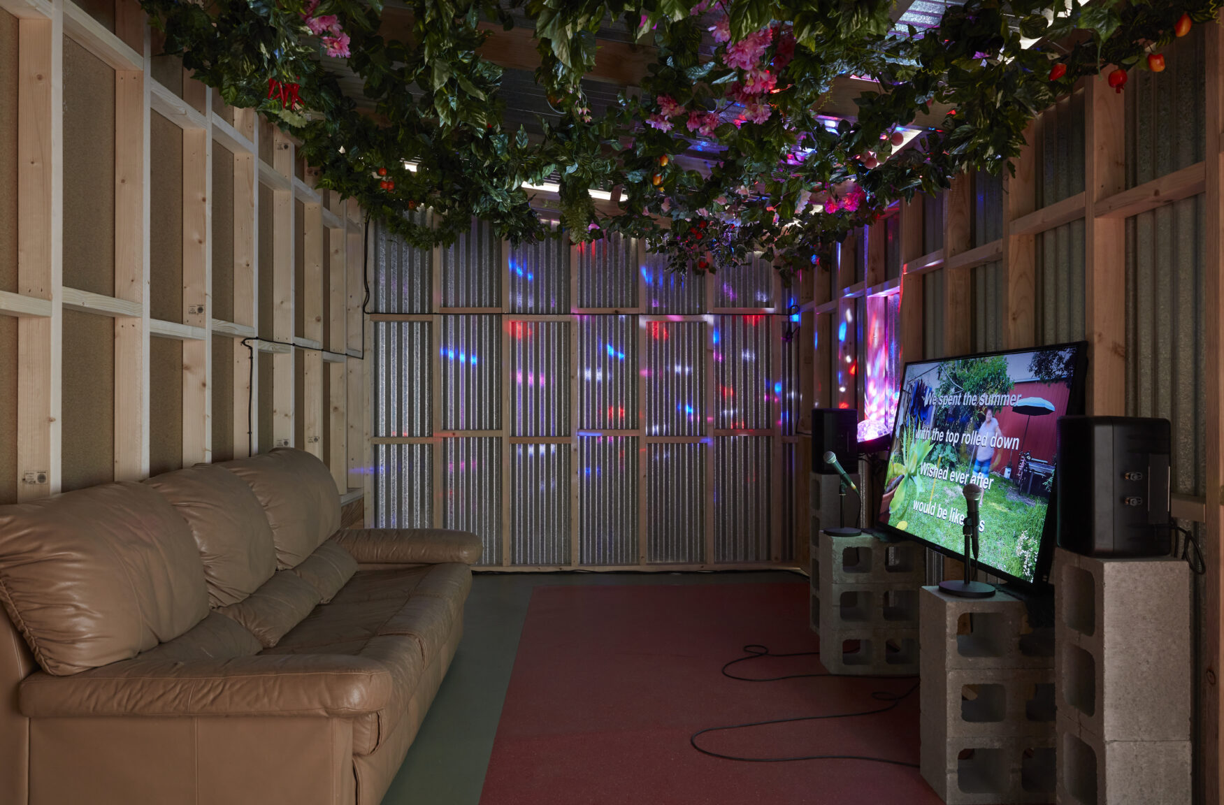 a karaoke room with tin walls, a leather couch, disco lights and a television with lyrics video