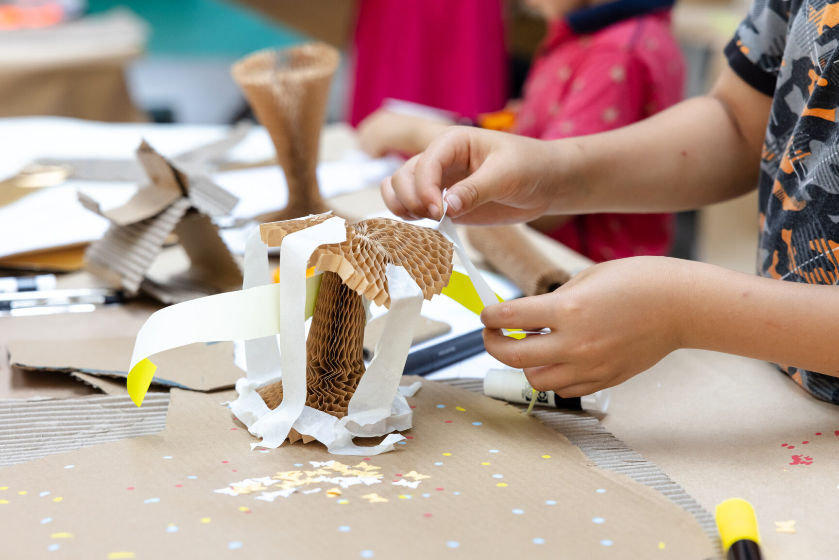 a child's hands working on a craft object made of paper and cardboard