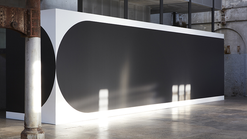 Large black shape painted on a white wall with light reflected onto the surface