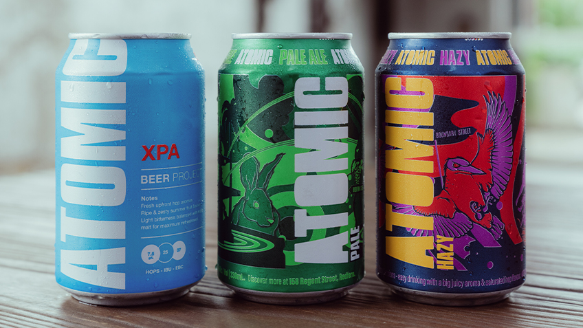 Three cans of Atomic beer lined up on a wooden table at Carriageworks