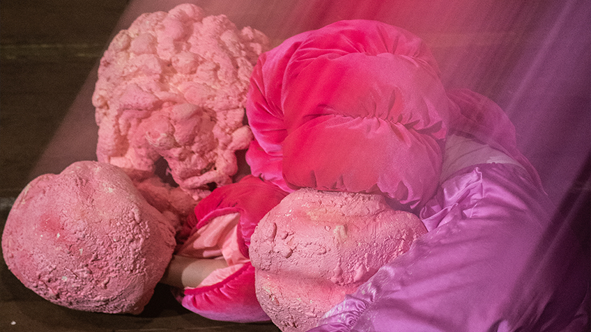 Amber McCartney lies on the ground in a puffy soft pink jacket. Her face and hands are obscured by rocky clay formations.
