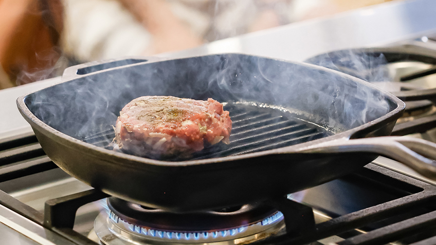A burger patty cooks on a grill
