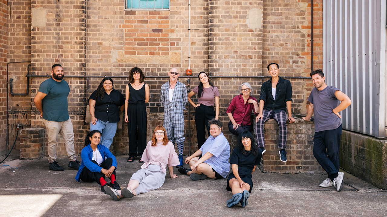 Twelve Clothing Store Artists pose in front of a brick wall of Carriageworks.