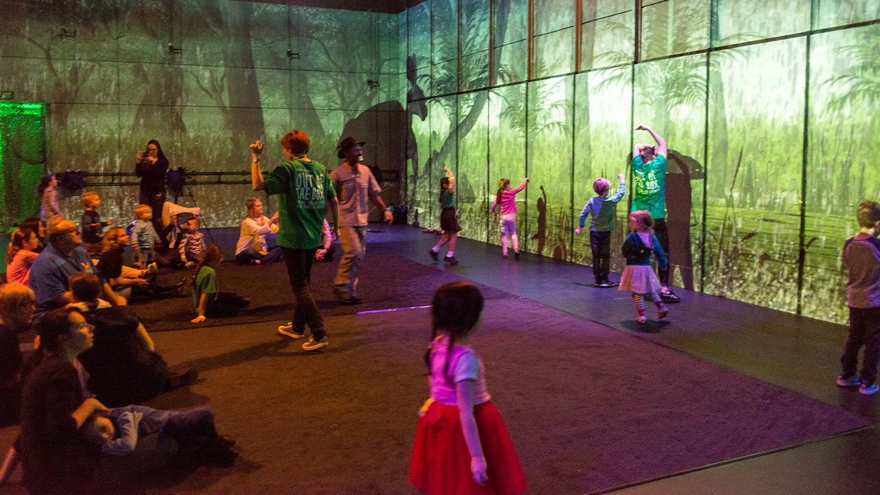 a group of children in a room with birds and forest images projected onto the walls