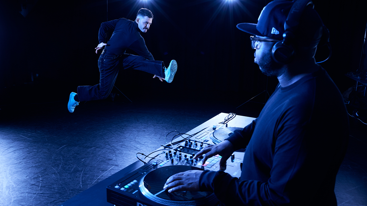 a person in a hat and headphones playing music on a turntable with another person breakdancing