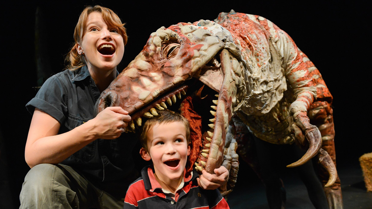 a person holding the jaws of a dinosaur open and child posing with their head in its mouth