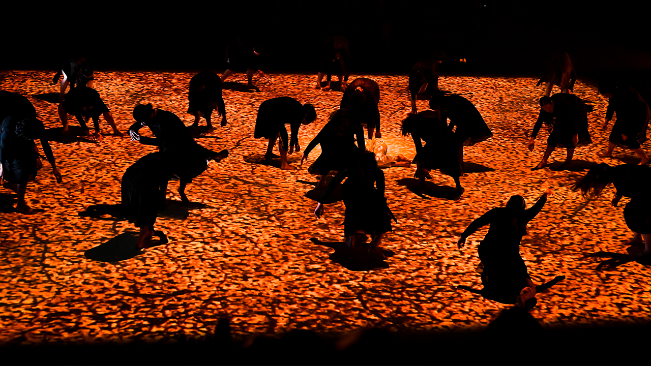 silhouettes of a groups of people dancing on a stage, with a light installation to look like a sandy surface
