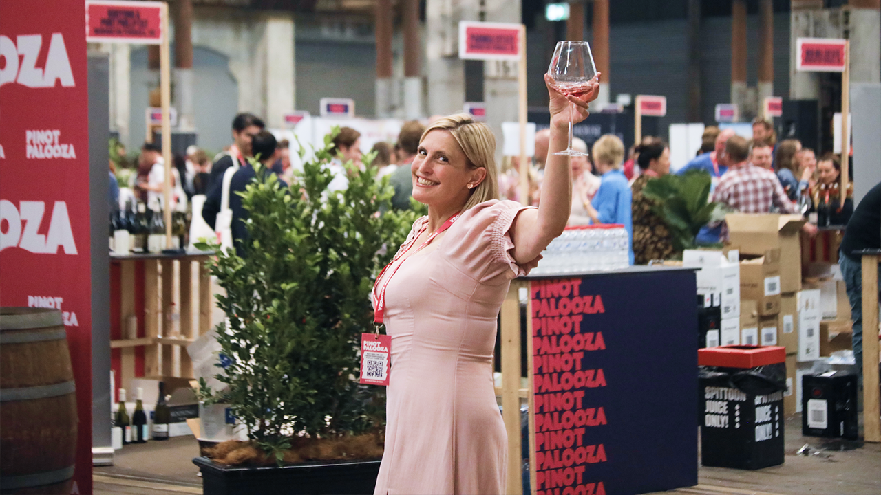 A woman in a pink dress raising a glass of red wine