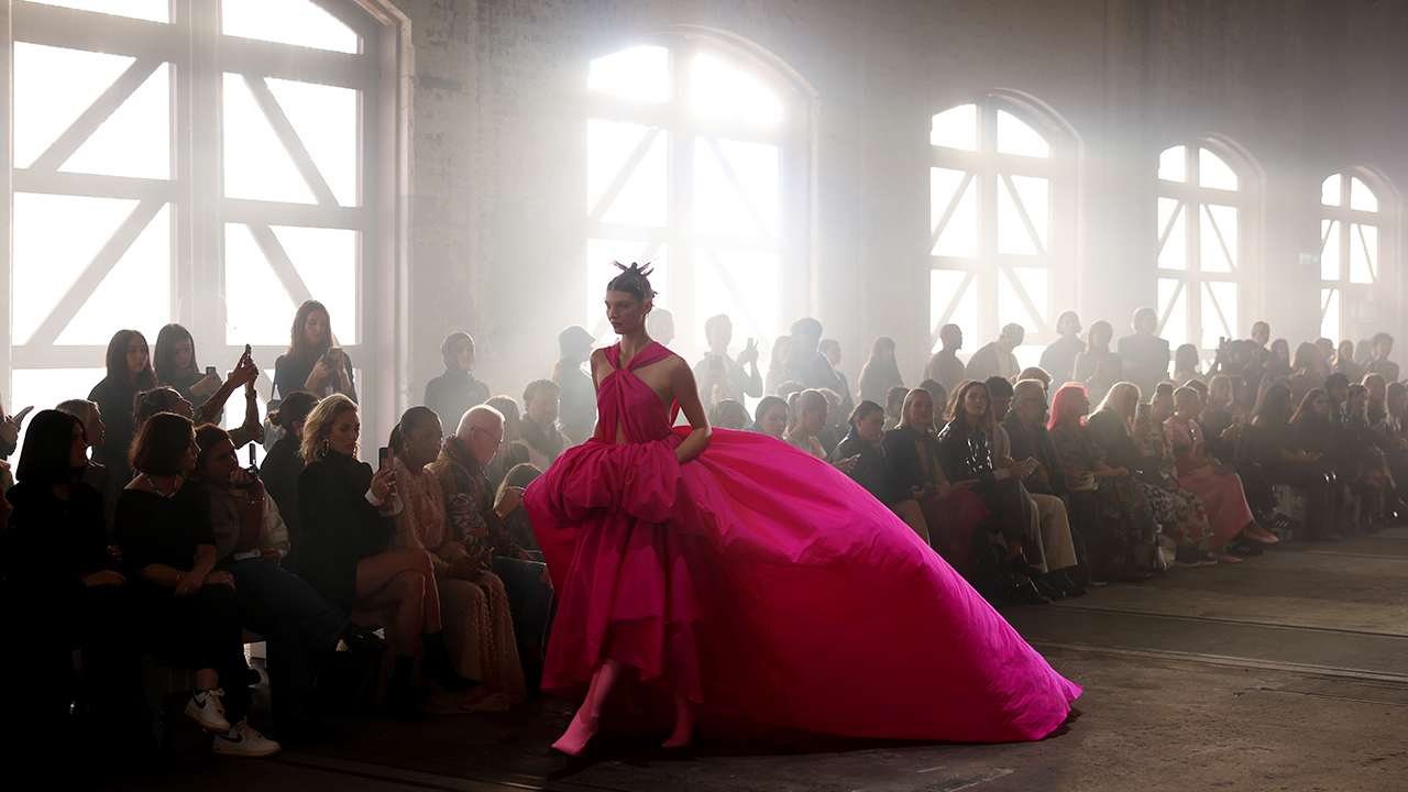 a model in a pink gown walking down a catwalk in front of a crowd of people