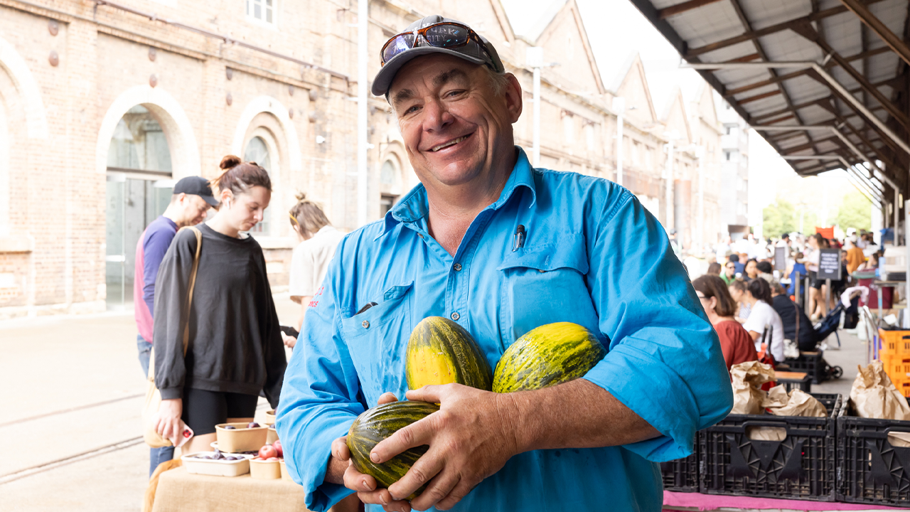 A man wearing a blue shirt holding three small melons