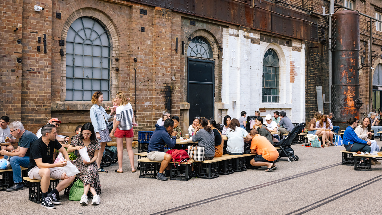 a group of people sitting at tables outside a refurbished industrial building