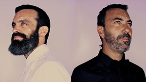 Two men with beards wearing black and white look in opposite directions with a pink background