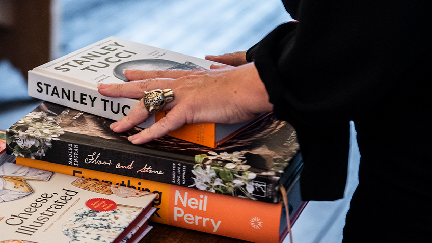 A hand with a leopard ring rests on a stack of three cookbooks