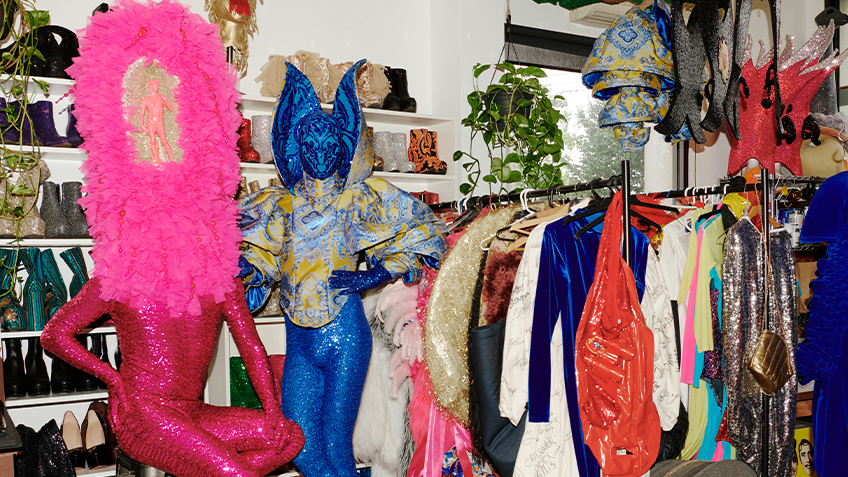 Will and Garrett Huxley stand in a pink and blue costume next to a rack of clothes in their studio.