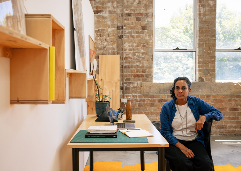 Keg De Souza sits at her desk in her Clothing Store Studio.