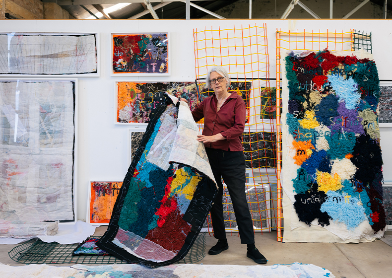 Liz Day stands in her Clothing Store studio holding one of her artworks
