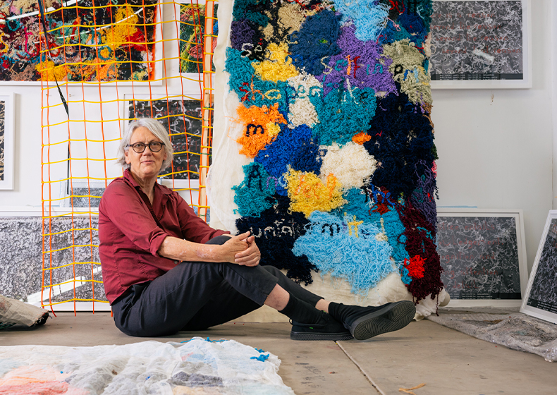 Liz Day sits on the floor in her studio next to one her art pieces.