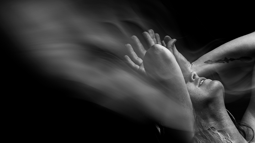 A black and white blurred image of someone looking up with their hands resting on their head.