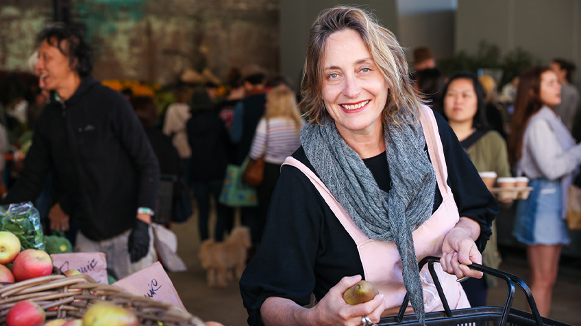 Alex Herbert grabs a pear at Carriageworks Farmers Market. She is holding a black shopping basket in the other hand.