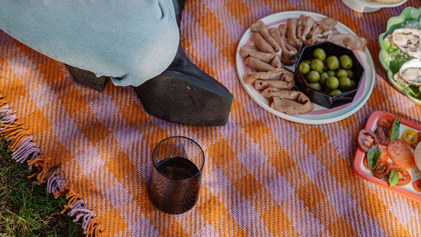 A foot. charcuterie and a glass of red wine sit on a PEEK NEEK picnic blanket