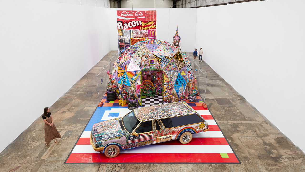A hearse sits in front of a geodesic dome and a tower as part of Paul Yore's exhibition WORD MADE FLESH