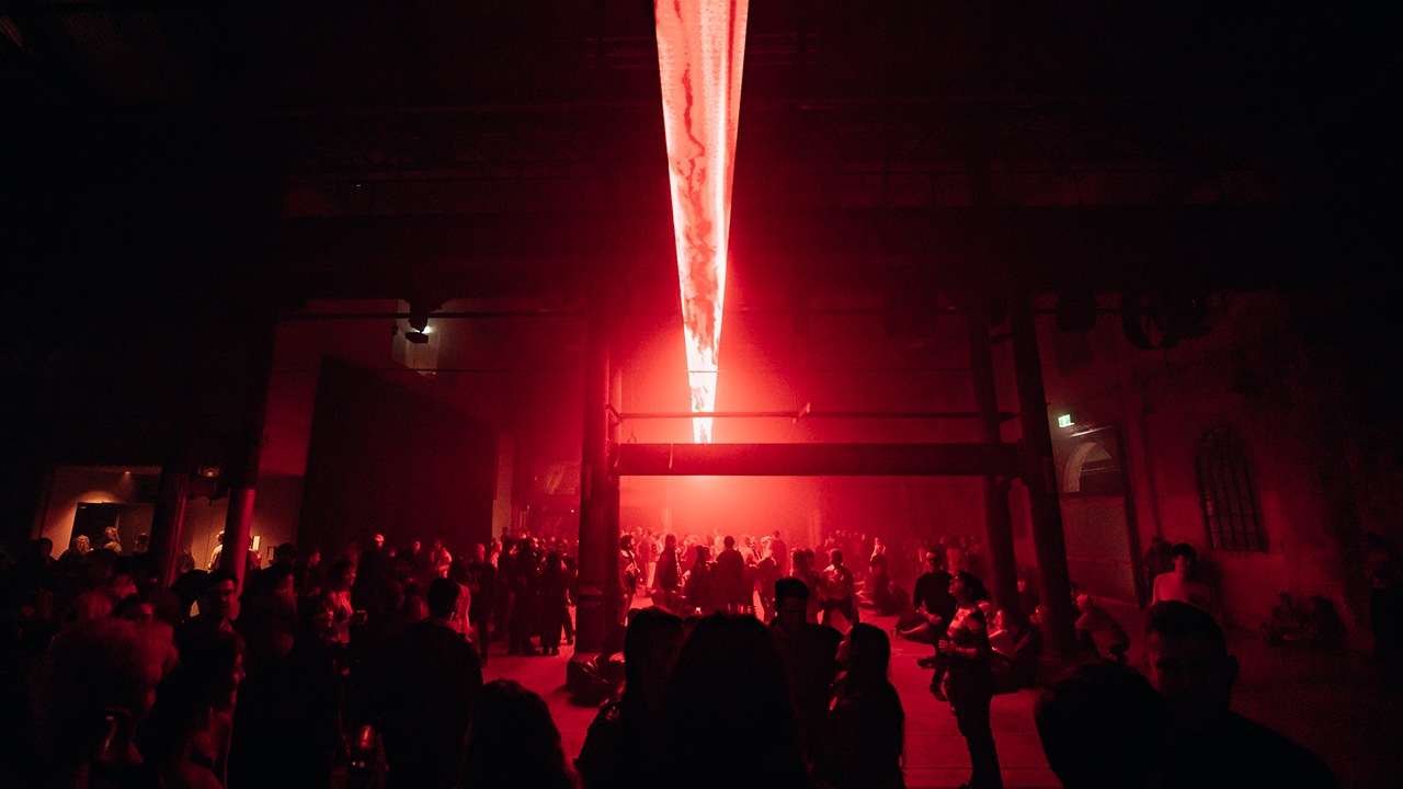 In a dark hazy room, a crowd socialises beneath a striking red light installation.