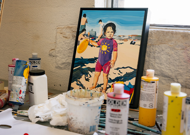A painting by Thea Perkins sits on a workbench with paint bottles in front.